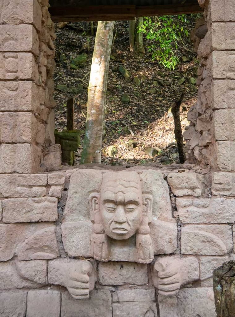 Intricate Maya masks carved beneath a palace window at the Copán UNESCO archaeological site — a highlight of the Copán day tour from Guatemala City by air for travelers who fly from Guatemala to Copán.