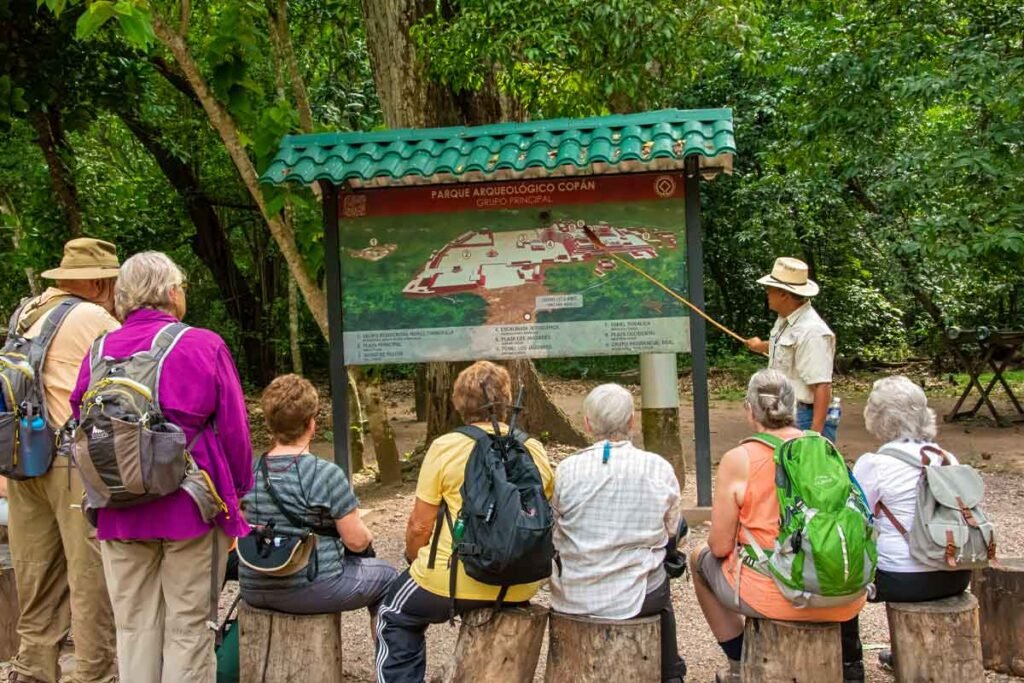 Small group of travelers listening to an expert guide explain the history of the Copán ruins during a Copán day tour from Guatemala City by air — a unique experience for those who fly from Guatemala to Copán.