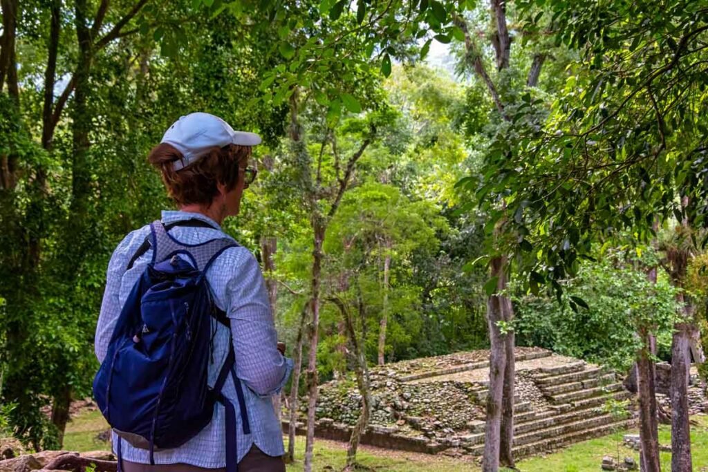 Traveler admiring an ancient Maya temple surrounded by lush rainforest at the Copán UNESCO archaeological site during a Copán day tour from Guatemala City by air.